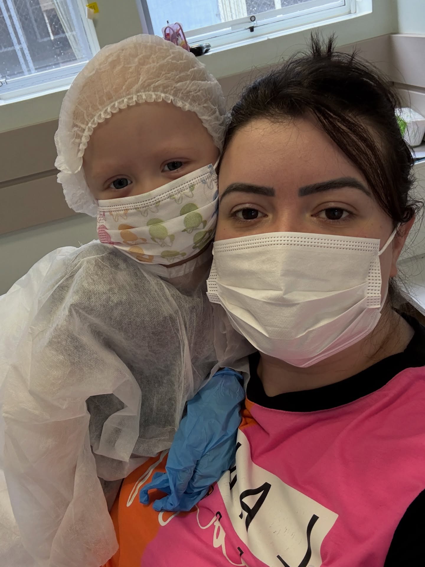 Olivia in a surgical cap, mask and gown, held close by her mother