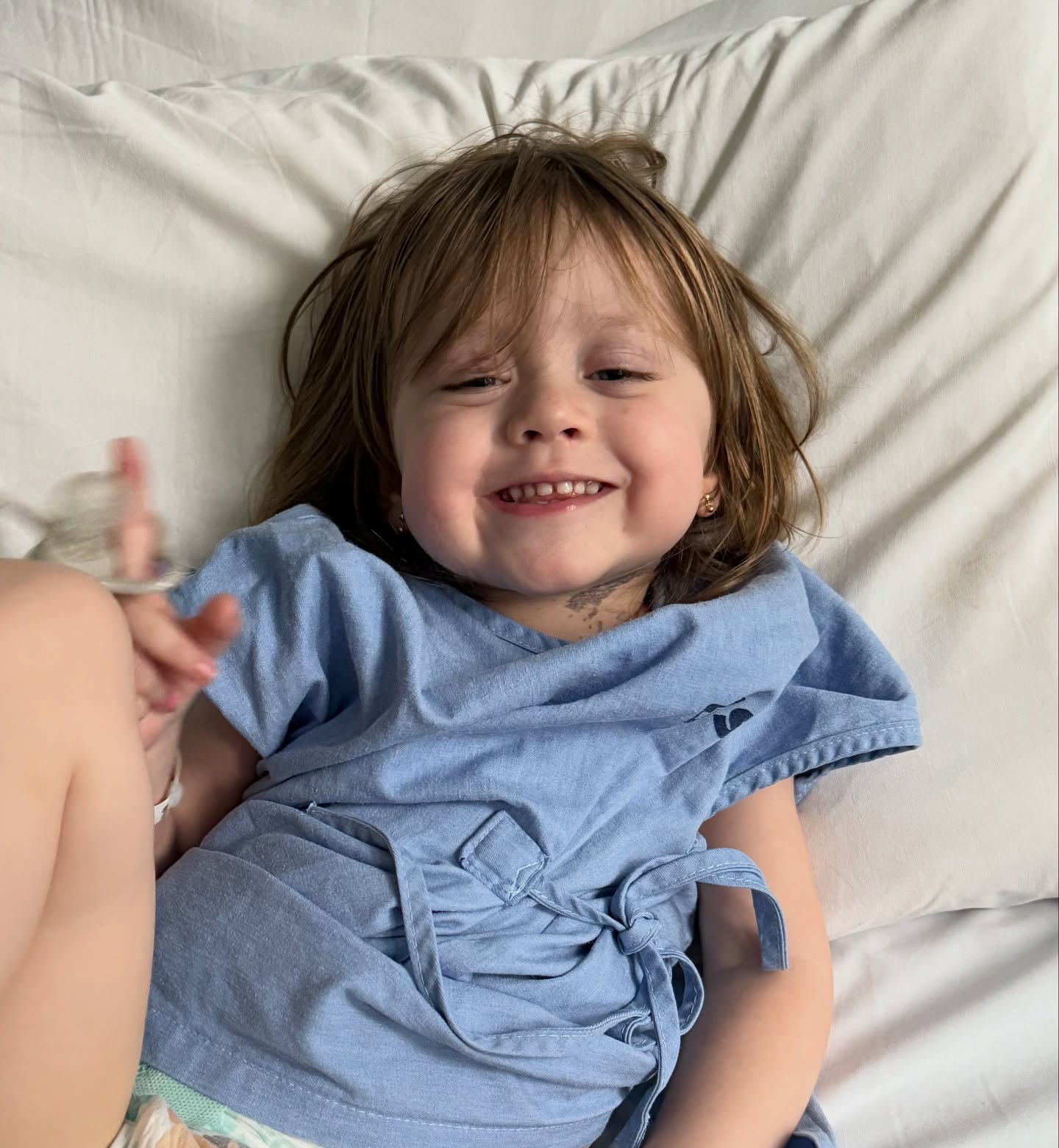 Olivia lying on a hospital bed in a blue gown, smiling